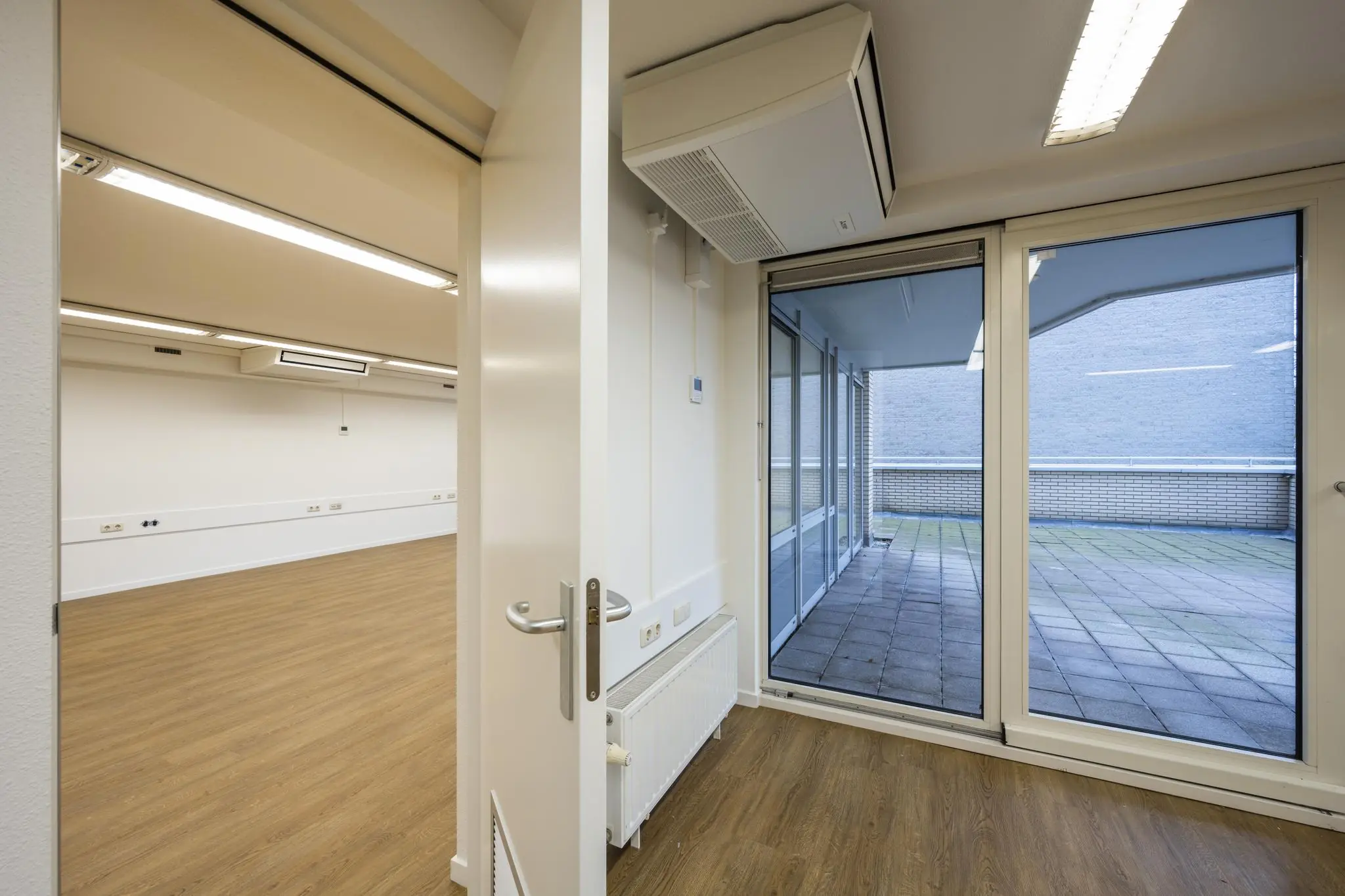 Licht kantoorruimte aan de Prins Hendrikkade met houten vloer, grote ramen en toegang tot een betegeld dakterras.